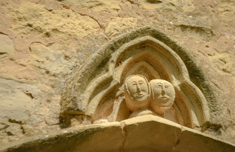 Close-up of ancient stone faces carved into a historic wall, showcasing medieval art.